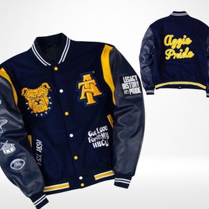 May include: Navy blue and yellow varsity jacket with leather sleeves. Features a bulldog graphic, the letters "A" and "T", and the words "Aggie Pride" on the back. Includes patches with text and symbols. The jacket has a striped collar, cuffs, and hem.