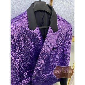 May include: A purple sequined blazer with a black collar and lapel. The jacket has a classic two-button closure and a single pocket. The sequins create a shimmering effect. The label reads "WESTERN CRAFT ATELIER HANDMADE."
