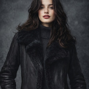 May include: A black leather jacket with a shearling collar and lining, worn over a grey turtleneck sweater. The woman has long, dark hair and is looking at the camera. The jacket is a classic style.