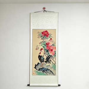 May include: A vertical scroll painting featuring a rooster and vibrant pink flowers. The rooster is black and white with a red comb, perched on a blue rock. The flowers are surrounded by green leaves against a cream background.