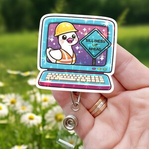 Könnte beinhalten: Ein Ausweis-Rollhalter mit einer Comic-Ente, die einen Bauhelm und eine Weste trägt, in einem Computerbildschirm. Der Bildschirm zeigt ein Schild mit der Aufschrift "Silliness Up Ahead". Der Rollhalter hat einen transparenten Kunststoffclip und eine einziehbare Schnur.