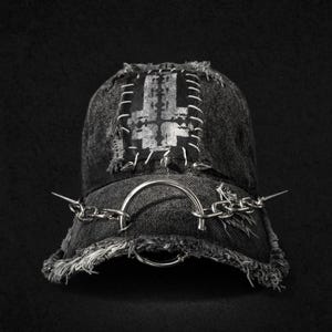 May include: A black denim baseball cap with a silver inverted cross patch and chain detailing. The cap has a distressed, frayed brim and is adorned with a silver ring and chain, and metal spikes.