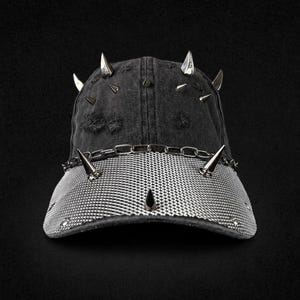 Può includere: Un cappellino da baseball in denim nero effetto vissuto con punte in metallo argentato sulla corona e sulla visiera. Una catena in metallo argentato è fissata alla base della corona e la visiera è rivestita da una sottile rete metallica.