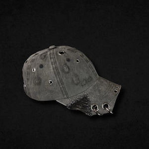 Könnte beinhalten: Eine anthrazitfarbene Baseballkappe im Used-Look mit mehreren silberfarbenen Metallösen und Ringen am Schirm und an der Kappe. Der Stoff hat eine verwaschene Optik mit ausgefransten Kanten und kleinen, absichtlichen Rissen im gesamten Design.