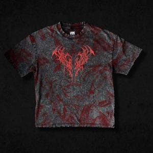 Könnte beinhalten: Grau-rotes T-Shirt mit Batikmuster und einem roten Tribal-Design auf der Vorderseite. Das Shirt hat kurze Ärmel und einen Rundhalsausschnitt. Der Text "LOORS" ist auf der oberen rechten Seite des Shirts aufgedruckt.