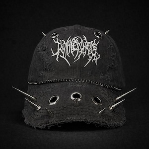 Könnte beinhalten: Schwarze Baseballkappe aus Denim mit Distressed-Details, Metallösen und silbernen Stacheln. Die Kappe hat einen weißen gestickten Text und eine Kette. Ein dunkles, kantiges Accessoire.