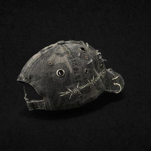 Könnte beinhalten: Eine Baseballkappe aus abgenutztem Denim mit Camouflagemuster. Die Kappe hat Metallösen, Stacheldrahtstickereien und silberne Reifenakzente. Der Schirm ist gebogen und die Kappe hat einen verstellbaren Riemen.