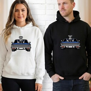 May include: White and black hooded sweatshirts with a graphic of a blue muscle car. The car has a detailed engine and is set against a white brick wall. The sweatshirts have a front pocket and a drawstring hood.