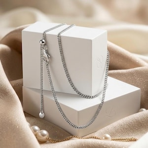 May include: A silver-toned curb chain necklace featuring a sliding adjustable bead mechanism and a lobster claw clasp. The chain includes a small dangling charm at the end of the adjustable section, showcasing a polished metallic finish throughout.