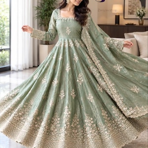 May include: A sage green floor-length gown with long sleeves and a square neckline, featuring intricate silver embroidery and beadwork throughout the bodice, skirt, and matching dupatta. The Zariyaa shop logo is visible in the upper right corner.
