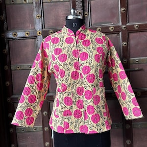 May include: A quilted jacket with a beige background and a repeating pattern of pink floral designs. The jacket has a mandarin collar, long sleeves, and two front pockets. The jacket is buttoned up and displayed on a mannequin.
