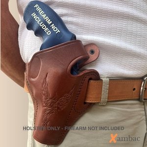 Könnte beinhalten: Ein braunes Lederholster mit geprägtem Phönix-Design, getragen an einem beigen Gürtel. Das Holster enthält ein blaues Trainingsgerät mit dem Text FIREARM NOT INCLUDED. Das Bild enthält zudem den Text HOLSTER ONLY - FIREARM NOT INCLUDED.