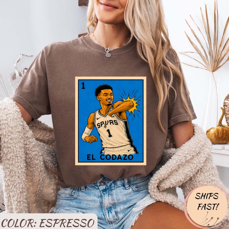 May include: Espresso-colored t-shirt featuring a graphic of a basketball player in a Spurs jersey. The graphic is in a blue frame with the text "EL CODAZO". The shirt is a comfortable, casual style.