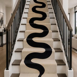 Op de afbeelding: Een beige tapijtloper voor de trap met een doorlopende, lange zwarte slangafbeelding die van de onderste trede naar boven slingert. De slang heeft een duidelijke kopvorm aan de onderkant en een slank, golvend lichaamspatroon.