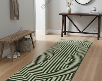 Puede incluir: Una alfombra rectangular con estampado geométrico verde y crema. La alfombra presenta un diseño repetitivo de líneas y formas angulares. La alfombra está colocada sobre un suelo de madera en un pasillo.