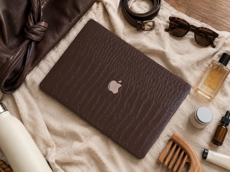 K&ouml;nnte beinhalten: Eine dunkelbraune Laptop-H&uuml;lle mit strukturierter Krokodilleder-Optik auf einem geschlossenen Laptop mit silbernem Apple-Logo. Die Folie bedeckt die gesamte Oberseite des Ger&auml;ts und verleiht ihm eine haptische Oberfl&auml;che mit reptilienartigem Muster.