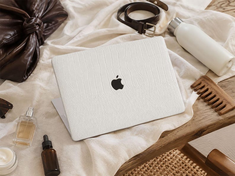 May include: A white laptop skin with a textured, embossed pattern applied to the lid of a closed laptop. The skin features a matte finish and covers the surface while leaving the black Apple logo visible in the centre of the device lid.