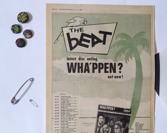 Puede incluir: Un anuncio de periódico vintage para la banda "The Beat" promocionando su último álbum "Wha'ppen?" El anuncio presenta una palmera de dibujos animados y un loro. La portada del álbum se muestra en la esquina inferior derecha del anuncio.