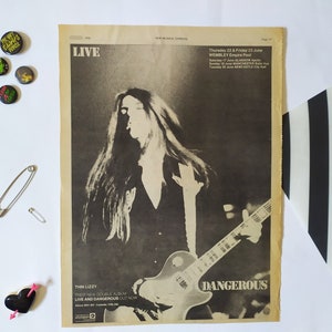 May include: A black and white photo of a musician playing a guitar. The photo is from a newspaper advertisement for a Thin Lizzy concert. The text reads "LIVE", "Thin Lizzy", "Their new double album LIVE AND DANGEROUS out now", "DANGEROUS", "Thursday 22 & Friday 23 June WEMBLEY Empire Pool", "Saturday 17 June GLASGOW Apollo", "Sunday 18 June MANCHESTER Apollo", "Tuesday 20 June NEWCASTLE City Hall".