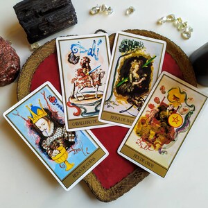 Puede incluir: Cuatro cartas de tarot con ilustraciones coloridas y texto en espa&ntilde;ol. Las cartas son "Caballero de Bastos", "Reina de Bastos", "Rey de Oros", y "Reina de Copas".