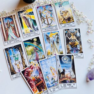 Peut inclure: Un jeu de cartes de tarot avec des illustrations color&eacute;es et du texte allemand. Les cartes sont dispos&eacute;es sur une surface blanche. Les cartes comprennent L'Ermite, La Roue de la Fortune, La Force, Le Diable, Le Pendu, L'&Eacute;toile et La Lune.