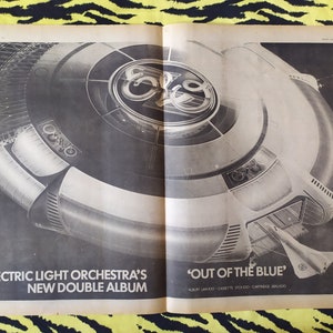 Peut inclure: Une publicité en noir et blanc dans un journal pour le nouvel album double d'Electric Light Orchestra, "Out of the Blue". La pochette de l'album présente un objet ressemblant à un vaisseau spatial avec un motif circulaire au centre.