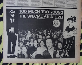 May include: A black and white poster advertising a concert by The Special AKA. The poster features a cartoon image of a man in a suit and a cartoon image of a woman holding a baby. The poster also includes the text "Too Much Too Young" and "The Special AKA Live!"