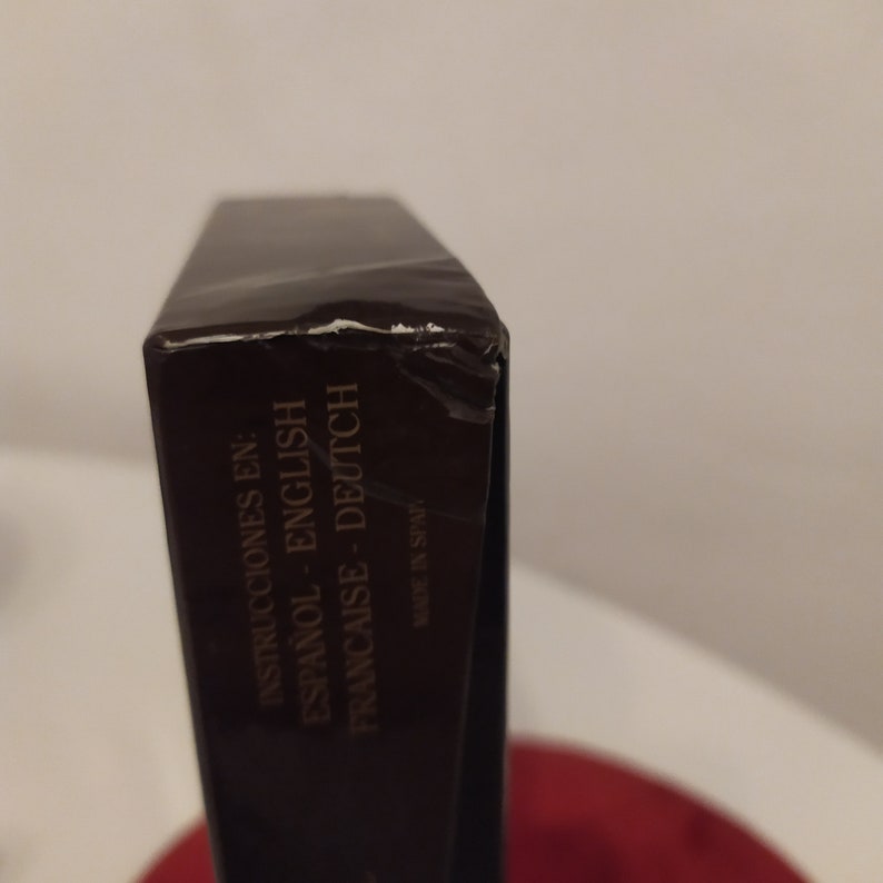 Puede incluir: Primer plano del lateral de una caja marr&oacute;n con el texto "Instrucciones en: Espanol - English Francaise - Deutsch" y "Made in Spain" impreso en ella.