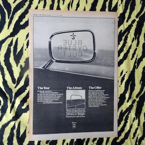 May include: A vintage advertisement for Blue Oyster Cult, featuring a car's side mirror reflecting the band's name. The ad includes tour dates and album information. The background is a black and yellow zebra print.