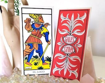 Puede incluir: Dos cartas de tarot rectangulares. Una carta presenta una ilustración colorida de una figura caminando con un bastón y un hatillo, etiquetada como EL LOCO. La otra tiene un fondo rojo con patrones florales blancos simétricos y el texto GALES S.A.