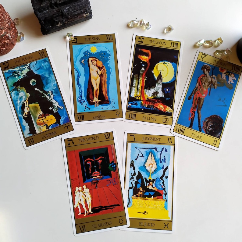 Puede incluir: Un juego de diez cartas de tarot con ilustraciones coloridas y bordes dorados. Las cartas presentan im&aacute;genes de una torre, una estrella, la luna, el mundo, el juicio, el sol y otros s&iacute;mbolos. Las cartas est&aacute;n etiquetadas con n&uacute;meros romanos y palabras en espa&ntilde;ol.