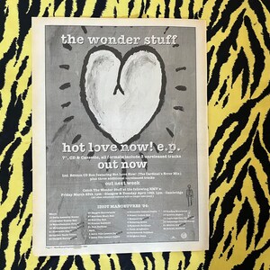 May include: A black and white advertisement for "the wonder stuff"'s "hot love now! e.p." featuring a heart graphic. The ad promotes the 7", CD, and cassette formats, including unreleased tracks. The ad also lists tour dates.