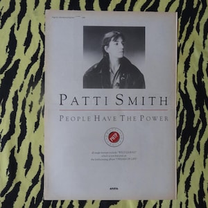 May include: A black and white photo of Patti Smith on a white background. The text "Patti Smith" and "People Have The Power" is printed in black. The text "PHP" is printed in red on a white circle.