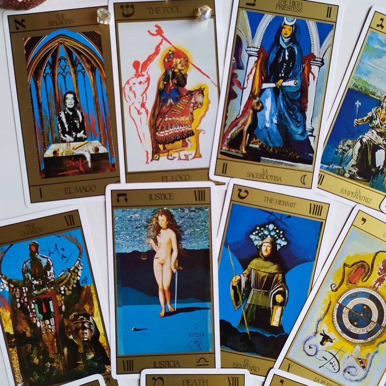 Puede incluir: Una baraja de tarot con bordes dorados e ilustraciones coloridas. Las cartas presentan im&aacute;genes del Mago, el Loco, la Sacerdotisa, la Emperatriz, la Justicia, el Ermita&ntilde;o, la Muerte y el Mundo.