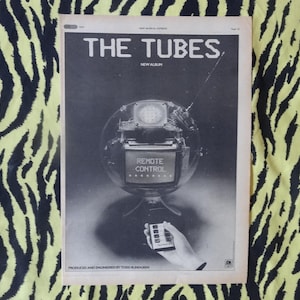 Könnte beinhalten: Eine Schwarzweiß-Zeitschriftenanzeige für das neue Album von The Tubes, "Remote Control". Die Anzeige zeigt ein roboterartiges Gerät mit einem Fernsehbildschirm, auf dem "Remote Control" steht.