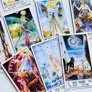 Peut inclure: Un &eacute;talement de cartes de tarot avec des illustrations color&eacute;es et du texte en allemand et en anglais. Les cartes comprennent L'Ermite, La Lune et L'&Eacute;toile.