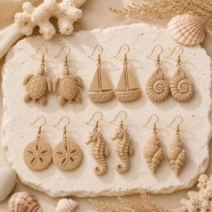 Op de afbeelding: Zes paar beige hangende oorbellen met nautische en mariene motieven, waaronder zeeschildpadden, zeilboten, spiraalschelpen, zanddollars, zeepaardjes en schelpen. Elke oorbel hangt aan een goudkleurige metalen haak.