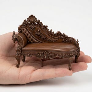 May include: A miniature brown chaise lounge featuring intricate carved wood detailing, a tufted backrest, and ornate floral motifs along the frame. The small furniture piece is designed with a curved silhouette and rests on four carved legs.