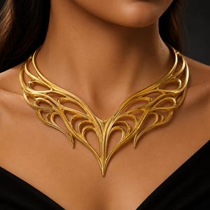 Op de afbeelding: Een goudkleurige statement ketting met een ingewikkeld, opengewerkt ontwerp met golvende, gebogen lijnen die in het midden een symmetrische, puntige V-vorm vormen. Het metaal heeft een gepolijste afwerking met gladde, afgeronde randen.