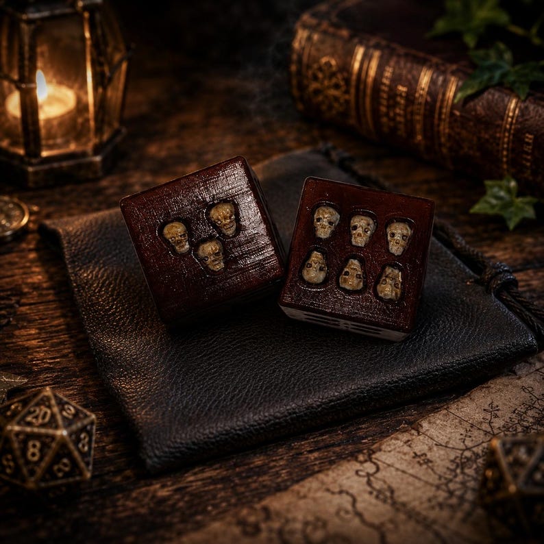 May include: Two dark brown square dice featuring small, off-white skull carvings embedded on their faces. One die displays three skulls, while the other die displays six skulls. The dice have a polished, wood-like finish and are resting on a black pouch.