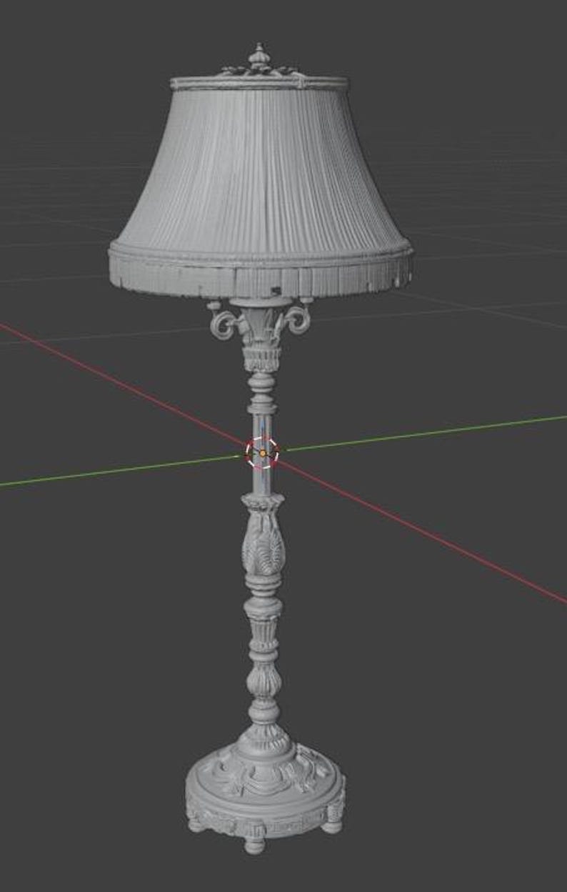 May include: A grey 3D digital model of a floor lamp featuring a pleated lampshade with a fringed bottom edge. The lamp stand is highly detailed with ornate carvings, a slender central column, and a wide, decorative circular base.