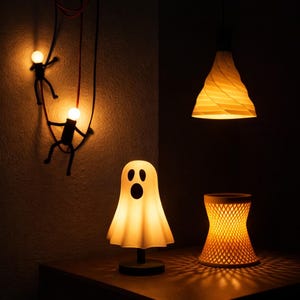 May include: A collection of illuminated decor items including a ghost-shaped lamp, a cylindrical lattice-patterned lamp, a white spiral pendant light, and two black stick-figure wall lamps with glowing bulbs, all emitting a warm yellow light.