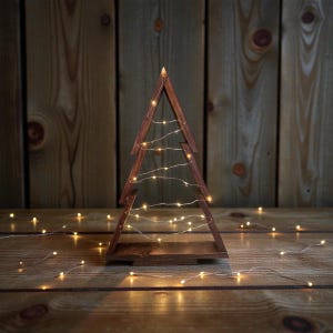 Könnte beinhalten: Ein Weihnachtsbaumschmuck aus Holz mit warmweißen Lichterketten. Der Baum besteht aus dunkelbraunem Holz und hat ein schlichtes, geometrisches Design. Die Lichter sind um den Baum herum angebracht und schaffen eine gemütliche, festliche Atmosphäre.