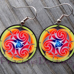 May include: A pair of round earrings with a colorful stained-glass design. The earrings feature a central swirl pattern in red, blue, and white, surrounded by orange and yellow hues. The earrings have silver-colored hooks.