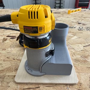 Puede incluir: Una fresadora eléctrica amarilla y negra de la marca DeWalt acoplada a una cubierta de extracción de polvo gris impresa en 3D. La herramienta incluye un cable de alimentación negro, una etiqueta de advertencia con texto y una base de madera.