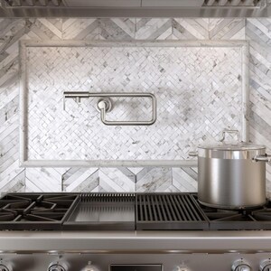 May include: Stainless steel pot on a gas stove with a black grate. A stainless steel paper towel holder is mounted on a white and gray tiled backsplash. The kitchen setting has a modern, clean aesthetic.