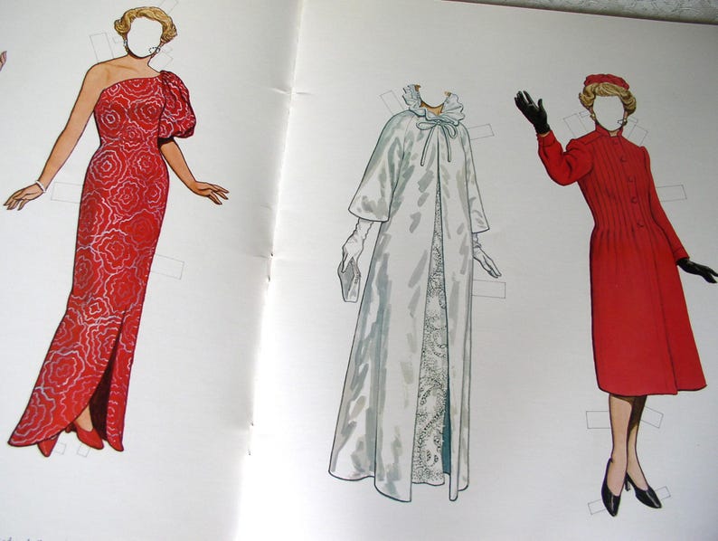 May include: A paper doll set featuring three figures with blank faces. The left figure wears a red one-shoulder gown with a white floral pattern. The center figure wears a long white coat with a ruffled collar. The right figure wears a red coat.