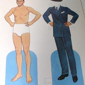 May include: A paper doll set featuring a male figure in white briefs and a separate blue pinstriped double-breasted suit with a matching fedora, white shirt, blue tie, and black shoes. The text reads The Twentieth Century Adonis and His first film: Love Is On the Air.