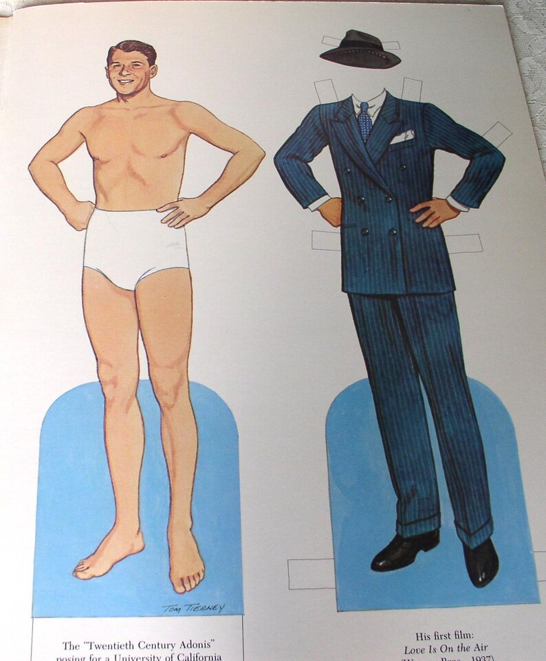 May include: A paper doll set featuring a male figure in white briefs and a separate blue pinstriped double-breasted suit with a matching fedora, white shirt, blue tie, and black shoes. The text reads The Twentieth Century Adonis and His first film: Love Is On the Air.