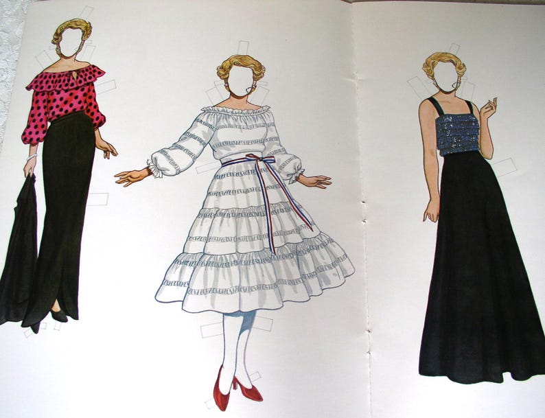 May include: A paper doll set featuring three figures with blonde hair and blank faces. The first wears a pink polka-dot blouse and black skirt. The second wears a white tiered dress with a red, white, and blue sash. The third wears a blue sequined top and black skirt.